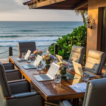 Outdoor conference table set with laptops overlooking the ocean at sunset.