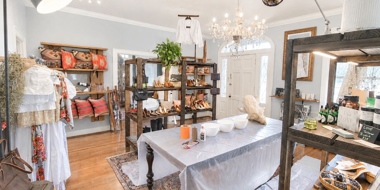 Bright boutique with shoes, clothing, and home decor items on rustic wooden shelves and racks.