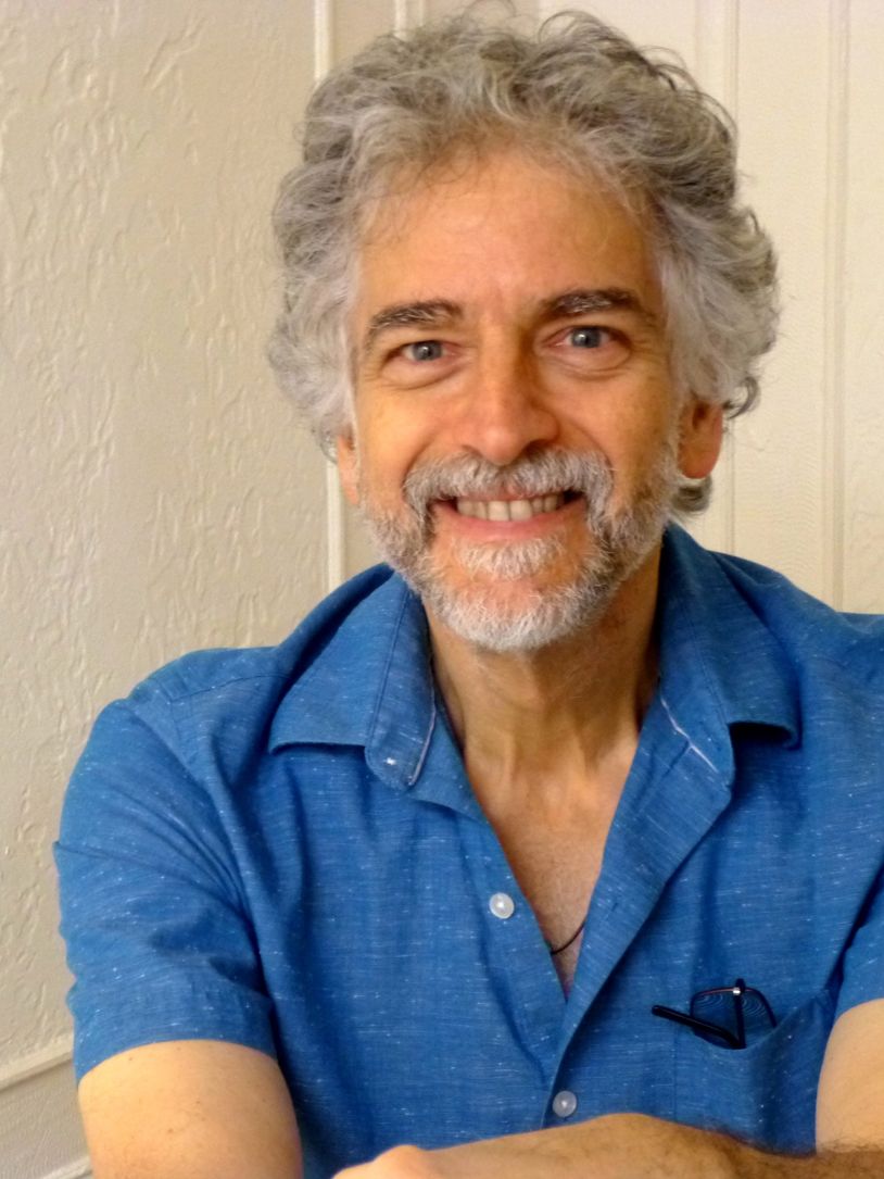 Smiling man with gray hair and beard in a blue shirt.