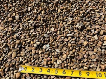 Measuring tape on a bed of small pebbles showing their size.