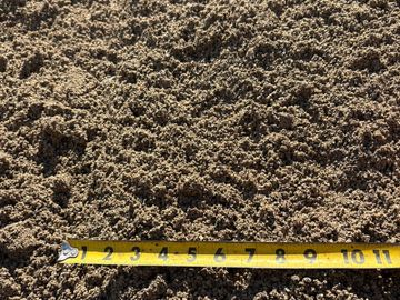 Close-up of sandy soil with a measuring tape laid across it.