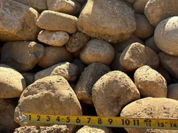 A pile of brown rocks with a measuring tape showing about 12 inches.