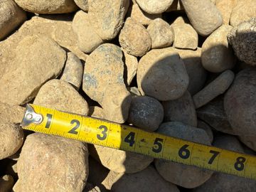 A measuring tape laid across various sized rocks outdoors.