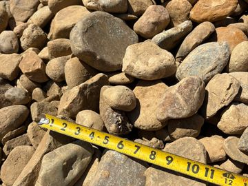 Measuring stones with a yellow tape measure under sunlight.