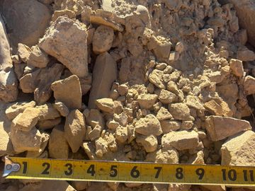 Yellow measuring tape over a pile of small, loose rocks and gravel.