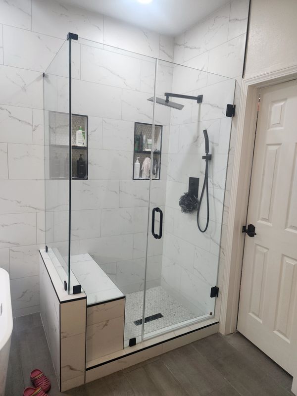Modern glass shower enclosure with marble tiles and built-in bench seating.