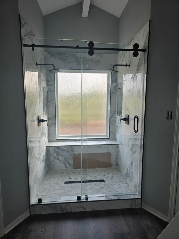 Modern walk-in shower with glass doors and marble tiles.