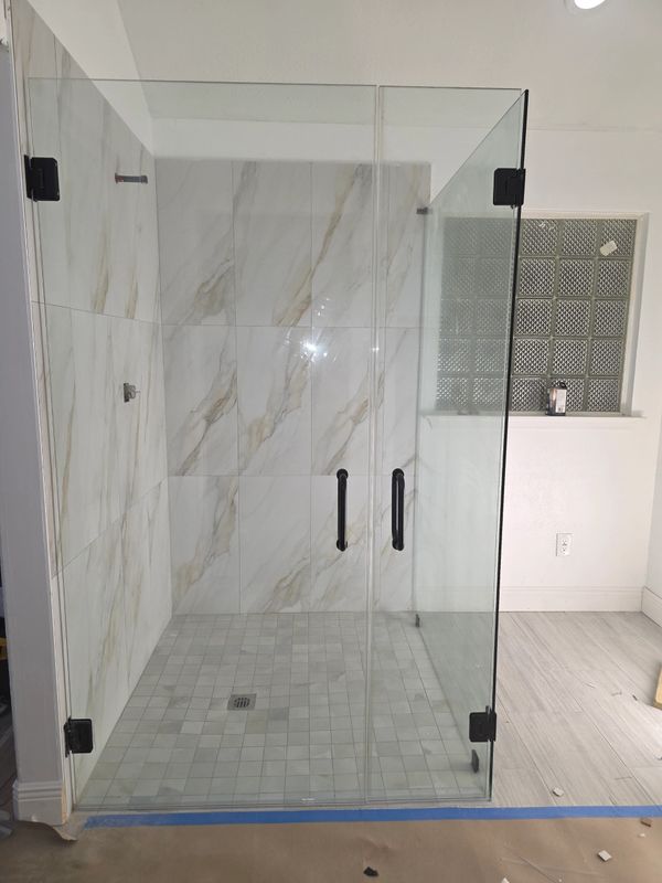 Modern glass shower enclosure with marble-patterned tiles and black handles.