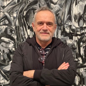 Man with folded arms standing in front of black-and-white abstract art.