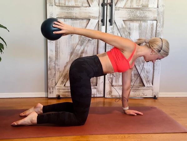 Woman exercising with a medicine ball on a yoga mat indoors.