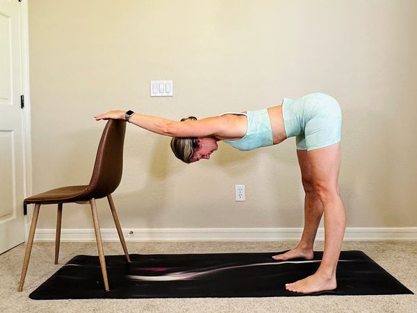 Woman stretching with arms on chair in a home workout.