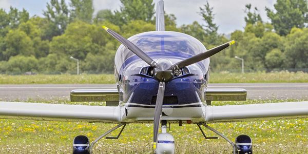 Front view of a small blue and white propeller airplane on grass.