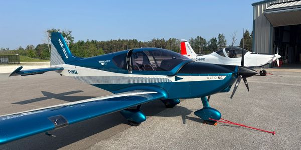 Small blue and white airplane parked on runway near hangar.