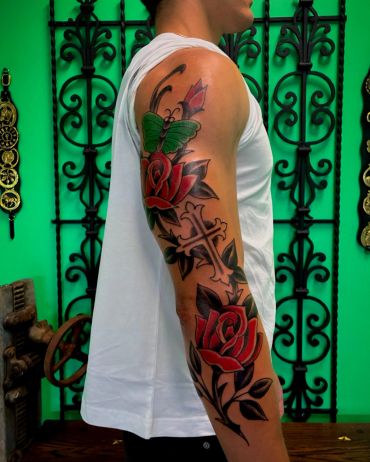 Colorful sleeve tattoo with roses, a cross, and a butterfly.