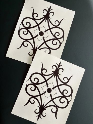 Two identical sheets with ornate black designs on white paper.