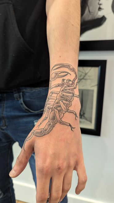 Detailed black and grey scorpion tattoo on the wrist and hand.