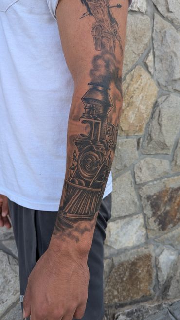 Detailed steam locomotive tattoo covering forearm with smoke effect.