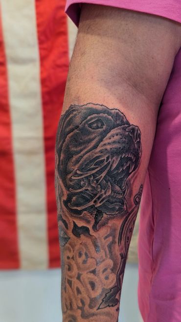 Black and grey tattoo of a fierce dog head on a forearm with text below.