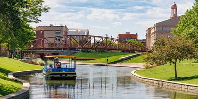 A blue tour boat cruises along a serene city canal under a red pedestrian bridge.
