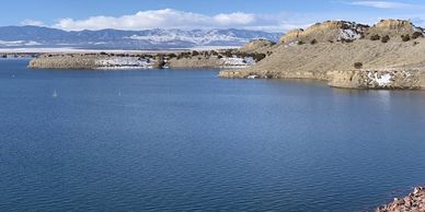 A serene lake with rocky shores and snow-dusted hills under a blue sky.