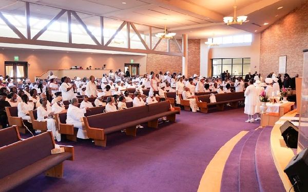 Congregation dressed in white attending a church service inside a spacious sanctuary.