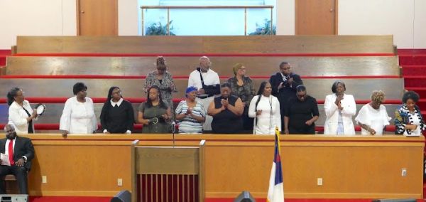 A choir singing inside a church with a pulpit and flag.