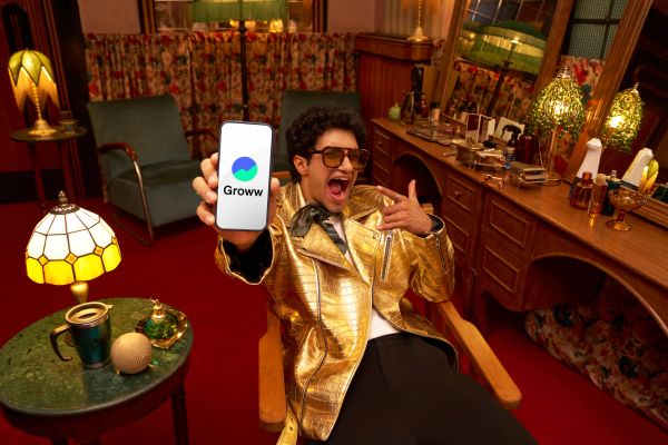 Excited person showing Groww app on phone in retro room.