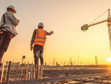Two construction workers inspect a building site at sunset.