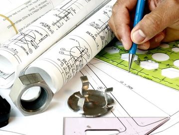 Hand drawing on technical blueprints with tools and nuts.