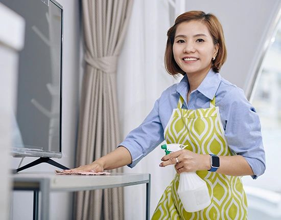 Woman cleaning a table with spray and cloth, smiling.
