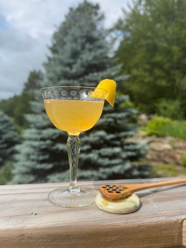 Elegant yellow cocktail with lemon twist on wooden railing, accompanied by honey dipper.