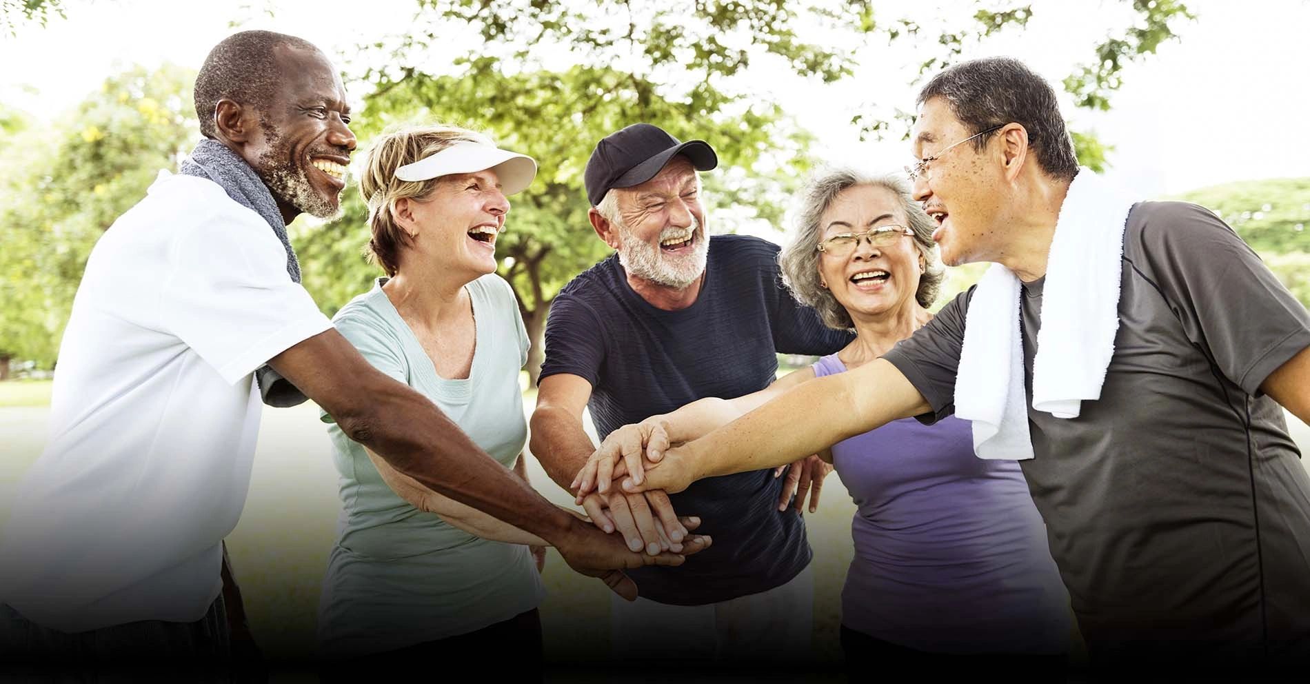 Group of happy seniors joining hands outdoors in a show of unity and friendship.