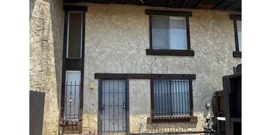 Exterior view of a beige stucco house with black-framed windows and metal bars.