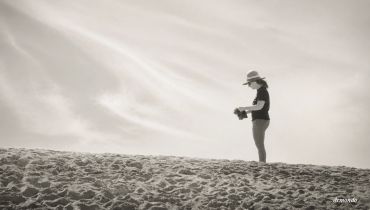Person standing alone on a sandy beach under a cloudy sky.