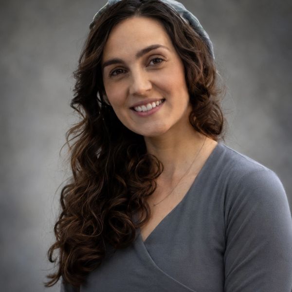 Smiling woman with long curly hair wearing a gray top and headband.