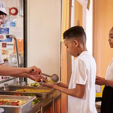 School children receiving lunch from cafeteria staff in a serving line.