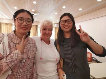 Three women smiling indoors, one showing a peace sign.