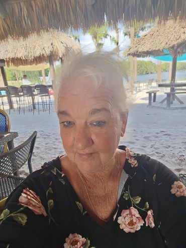 Woman taking a selfie at a beachside bar with thatched umbrellas.