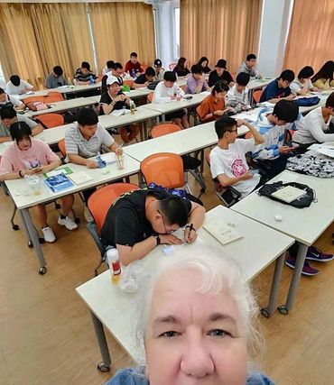 Teacher taking a selfie in a busy classroom full of students.