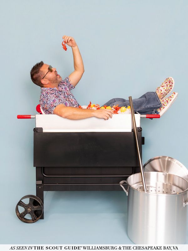 Man lounging in a cooler filled with seafood, eating a crab claw.