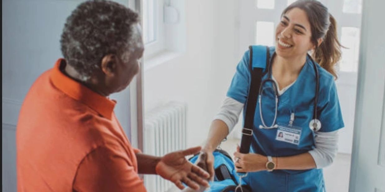 Nurse warmly greeting an elderly man at his door with a smile.