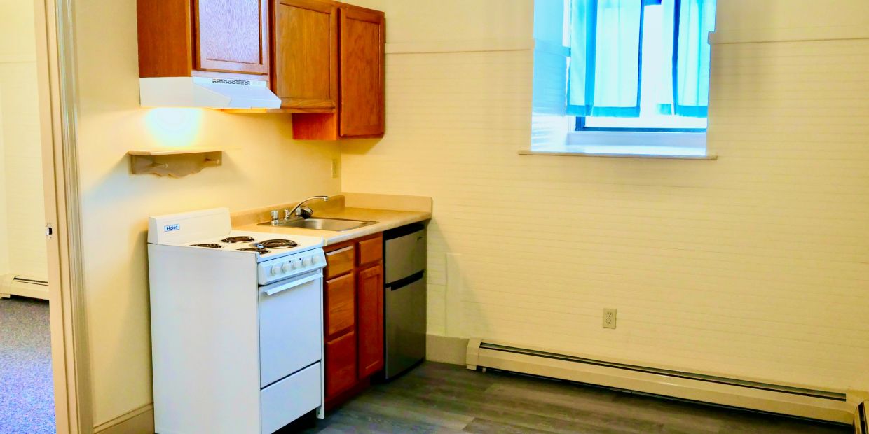 Small kitchen with wooden cabinets, white stove, and a window with blue curtains.