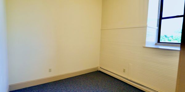 Empty room with beige walls, carpeted floor, and a window.