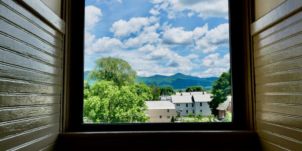 View of green trees and mountains through a window on a sunny day.