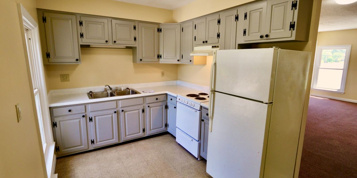 Compact kitchen with gray cabinets, white appliances, and a beige wall.