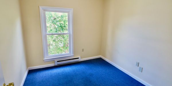 Empty room with blue carpet and a window letting in natural light.