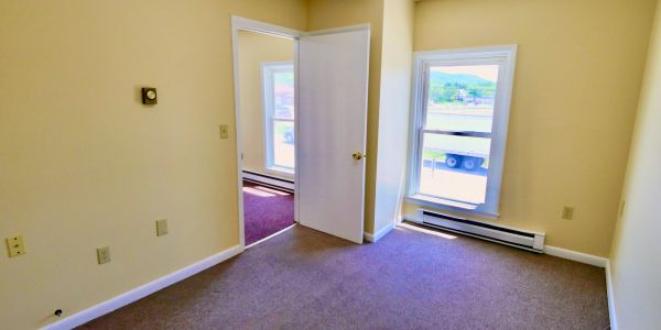 Empty room with beige walls, carpet, and open door leading to another room.
