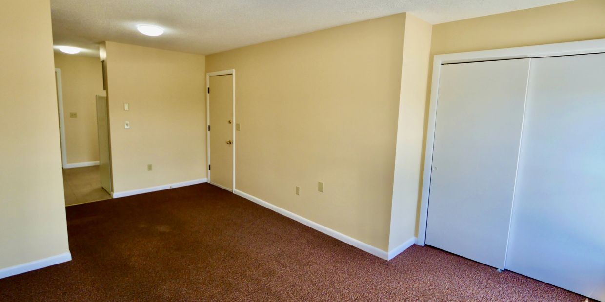 Empty room with beige walls, brown carpet, and white closet doors.