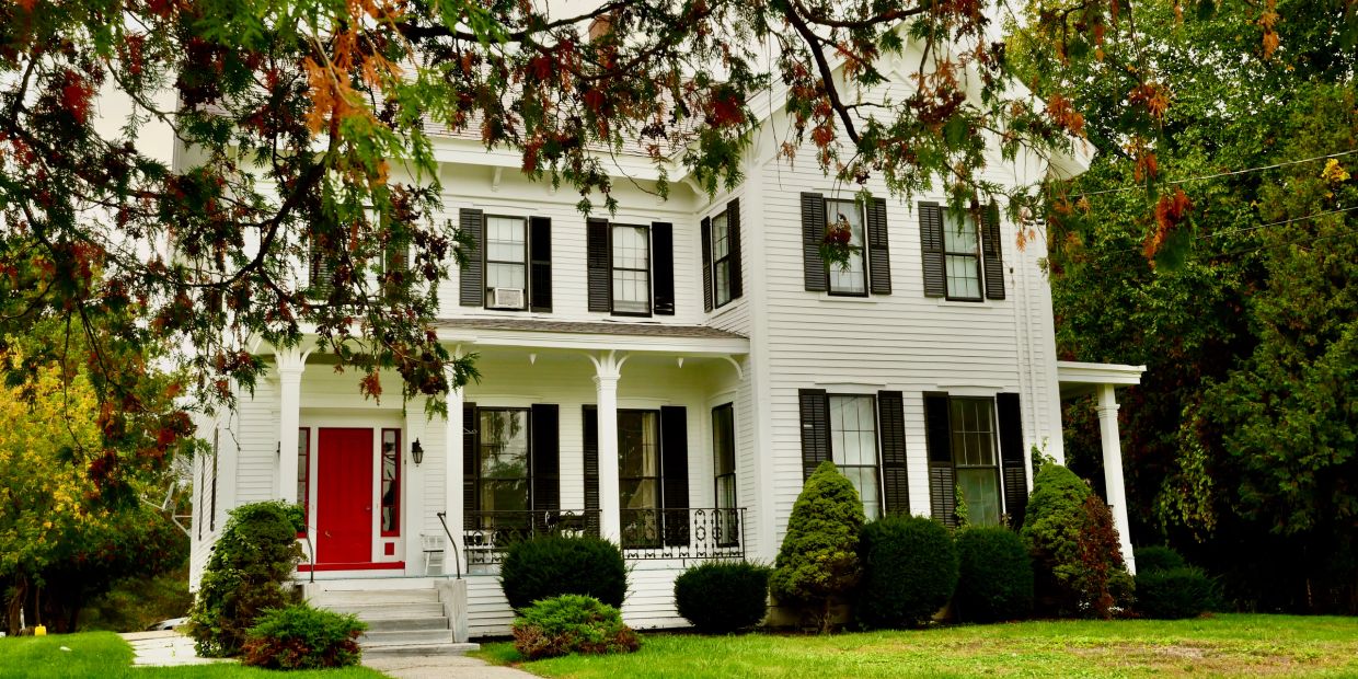 White house with a red door surrounded by greenery.