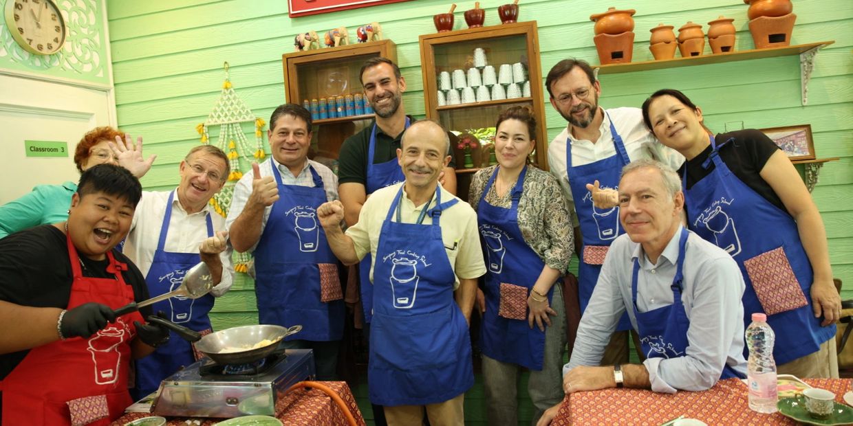 Group of people in aprons posing happily in a cooking class.